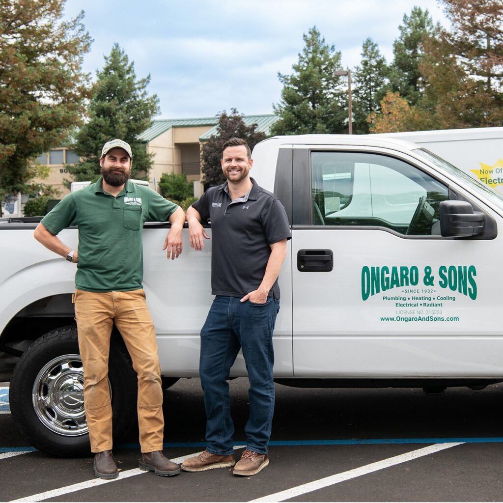 Two men are standing in front of a white pick up truck with the logo Ongaro & Sons on the side.