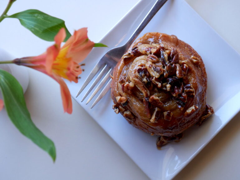 A pastry on a white plate and a flower on a white tablecloth