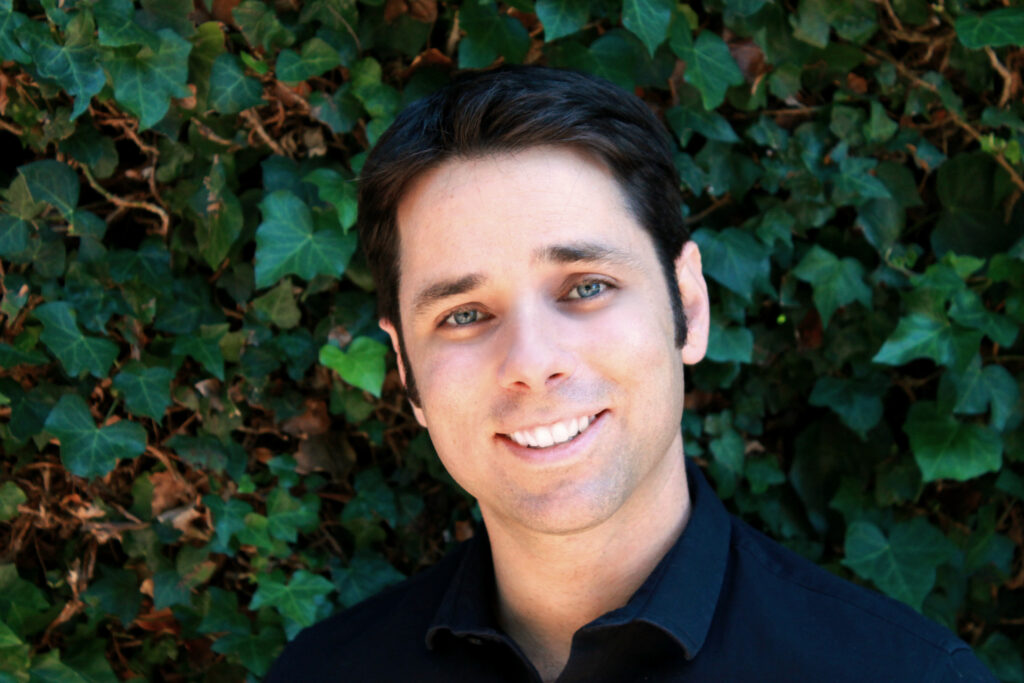 A man with black hair and blue eyes is smiling