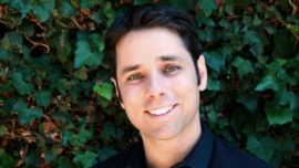 A man with black hair and blue eyes is smiling