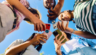 Friends gathered outdoors, smiling and holding smartphones
