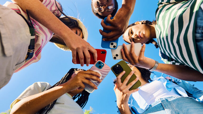 Friends gathered outdoors, smiling and holding smartphones