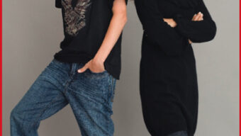 Two young people stand against a plain background. The person on the left, showing off their Head of the Class style, wears a black T-shirt, blue jeans, and a beanie, with one foot on a small stack of books. The person on the right, wearing a black dress and tights, stands with arms crossed, smiling.