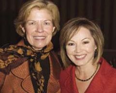 Two women are standing close to each other and smiling at the camera. The woman on the left, supporting the Foundation, has short, light hair and is wearing a patterned scarf and a brownish-orange jacket. The woman on the right has short, straight dark hair and is wearing a red jacket and a necklace reflecting her ARCS pride.