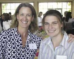 Two people are standing side by side, smiling at the camera. The person on the left is wearing a patterned shirt, and the person on the right is wearing a striped shirt. Both are indoors with large windows and other people in the background, capturing a perfect summer moment.
