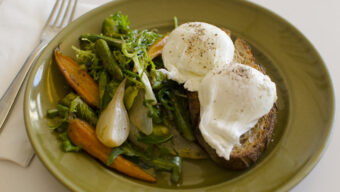 A green plate with poached eggs on whole grain toast, served with a side of mixed vegetables including carrots, green beans, and leafy greens. A fork and napkin are placed next to the plate—a perfect breakfast enjoyed by Marin locals.
