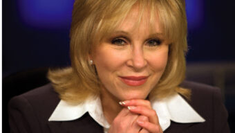 Cheryl Jennings, with shoulder-length blonde hair, is smiling slightly and resting her chin on her hands. She wears a dark blazer over a white shirt, while the background fades into a blue and purple gradient.