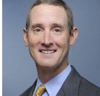 A man in a gray suit with a light blue shirt and yellow patterned tie is smiling. He has short, light brown hair and stands against a plain, gray background. Professional yet approachable, this image could be perfect for any "For Sale" advertisement needing a touch of class and confidence.