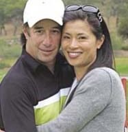A man wearing a white cap and black shirt with a green stripe and a woman in a gray sweater with sunglasses on her head are embracing and smiling, enjoying the outdoors. The scene has blurred greenery in the background, creating an atmosphere of natural accessibility and joy.
