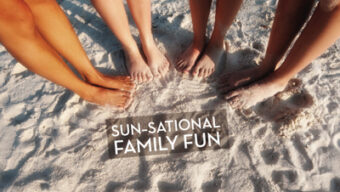 Four pairs of feet, of different sizes, are placed in a circle on sandy beach with the text "SUN-SATIONAL FAMILY FUN" written in the center. The sun-soaked scene captures a family enjoying a sunny day at the beach together in So Cal.