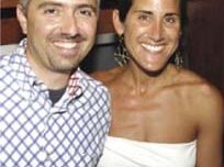 A smiling man and woman pose together indoors, radiating joy. The man, with short graying hair and a patterned shirt, stands closely next to the woman, whose long dark hair is pulled back. She's wearing a sleeveless white top. Both seem to be enjoying the moment, perhaps after attending an engaging arts salon in Marin.