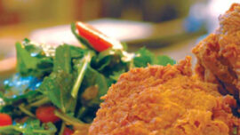 A close-up of a plate with crispy fried chicken, the epitome of comfort food, served next to a fresh salad with mixed greens and sliced red bell peppers. The background is softly blurred, drawing focus to the appetizing meal. Ideal for a cozy evening in Mill Valley.