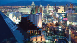 Aerial view of the Las Vegas Strip illuminated at night, showcasing the iconic Luxor pyramid on the left, a variety of brightly lit hotels, casinos, and the bustling city street below with numerous lights and neon signs against a dark mountain backdrop—a visual Strip search in neon splendor.