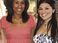 Two women are posing and smiling for a photo. The woman on the left is wearing a pink lace dress by Juicy Couture, and the woman on the right is wearing a strapless dress with a white, blue, and black pattern. They are standing indoors, with a blurred background.
