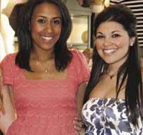 Two women are posing and smiling for a photo. The woman on the left is wearing a pink lace dress by Juicy Couture, and the woman on the right is wearing a strapless dress with a white, blue, and black pattern. They are standing indoors, with a blurred background.