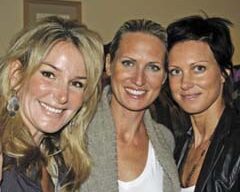 Three smiling people pose closely together indoors at a charming local Larkspur business. The individual on the left has long blonde hair, the one in the middle has light brown hair tied back, and the individual on the right has short dark hair. All three are dressed casually.