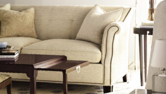A cozy, well-lit living room with a sensational beige sectional sofa and two matching chairs. A coffee table with a lift-top feature stands on a light carpet patterned with blue designs. The space is decorated with framed pictures, a side table, and a floor lamp.