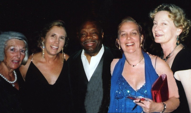 A group of five people dressed in formal attire stand together, smiling for the camera at the Spring Gala. Four women, wearing elegant dresses and accessories, surround a man in a suit and tie. The background is dark, making the group the focal point of the image.