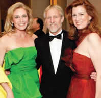 Three people are smiling and posing for a photograph at the Gala. The person on the left is wearing a green dress, the person in the middle is dressed in a black tuxedo, and the person on the right is wearing a red dress. They appear to be in a formal setting, possibly celebrating Russian Treasures of the San Francisco Ballet.