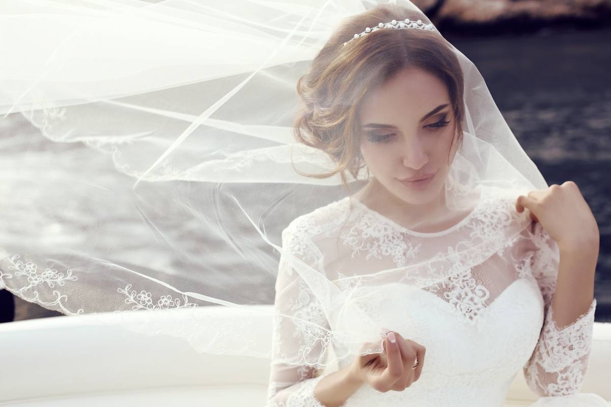 fashion photo of beautiful sensual bride with dark hair in luxurious lace wedding dress posing on yacht
