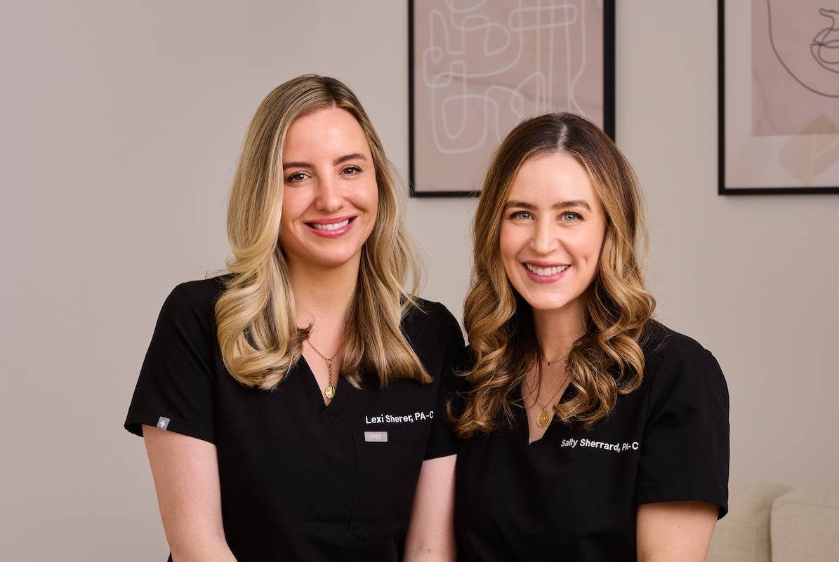 Two woman who work at a plastic surgery place smiling in uniform